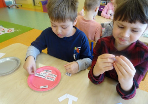 Dzieci czytają nazwy produktów spożywczych zapisanych na karteczkach.